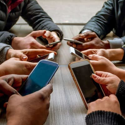 six sets of hands set up in a circle all holding various smartphone models as though they are texting