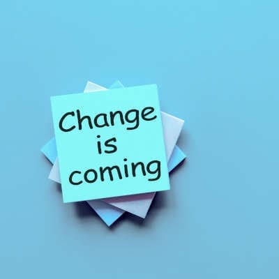 Light blue background, a stack of sticky note pads at the center, written on the top is "change is coming" in black lettering