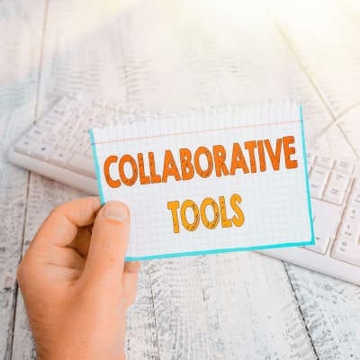 A white hand hold a white card with orange lettering that says 'collaborative tools.'
